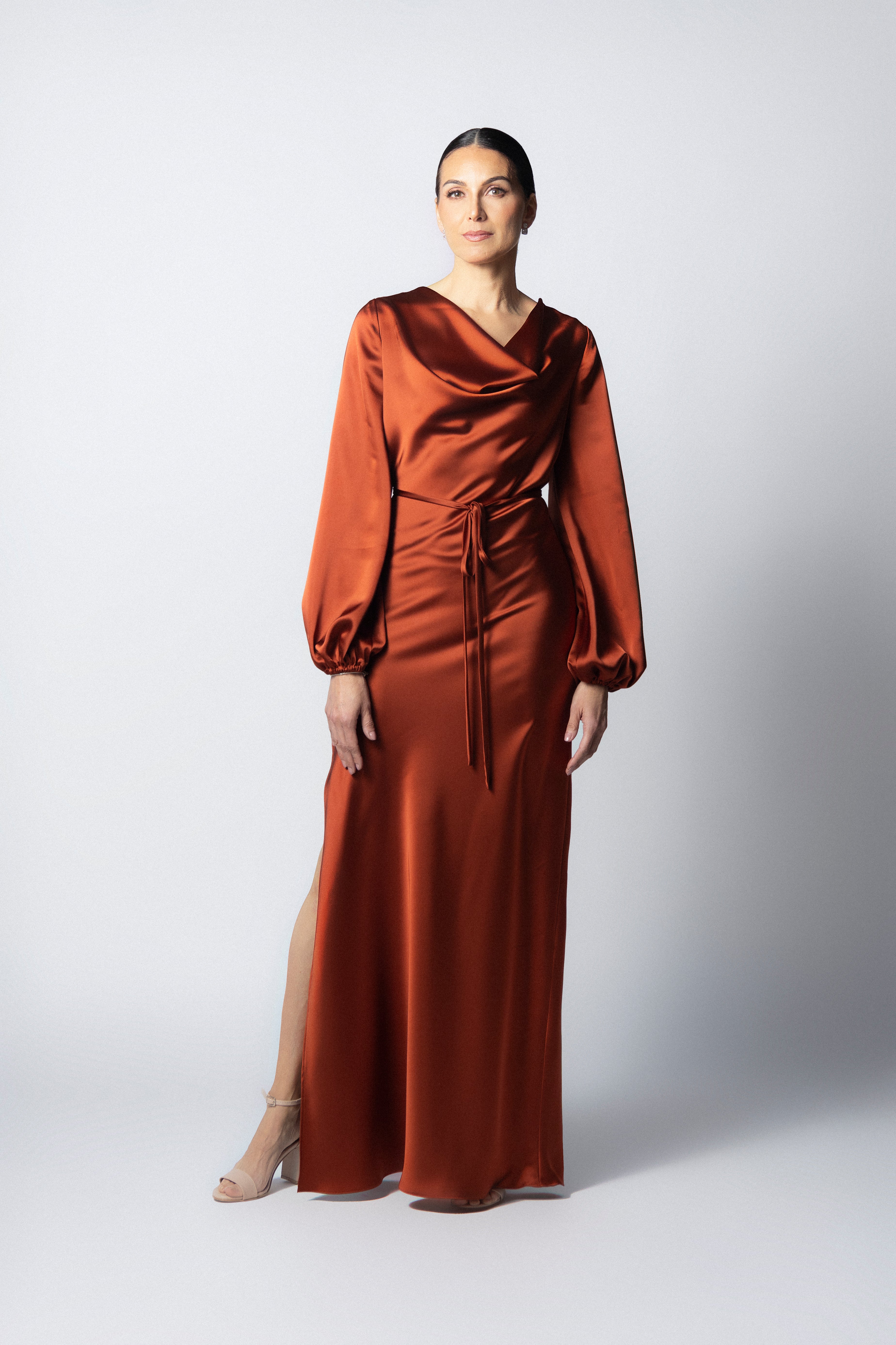 Vestido maxi de satín color óxido con cuello drapeado, mangas largas abullonadas y apertura lateral en la pierna.
