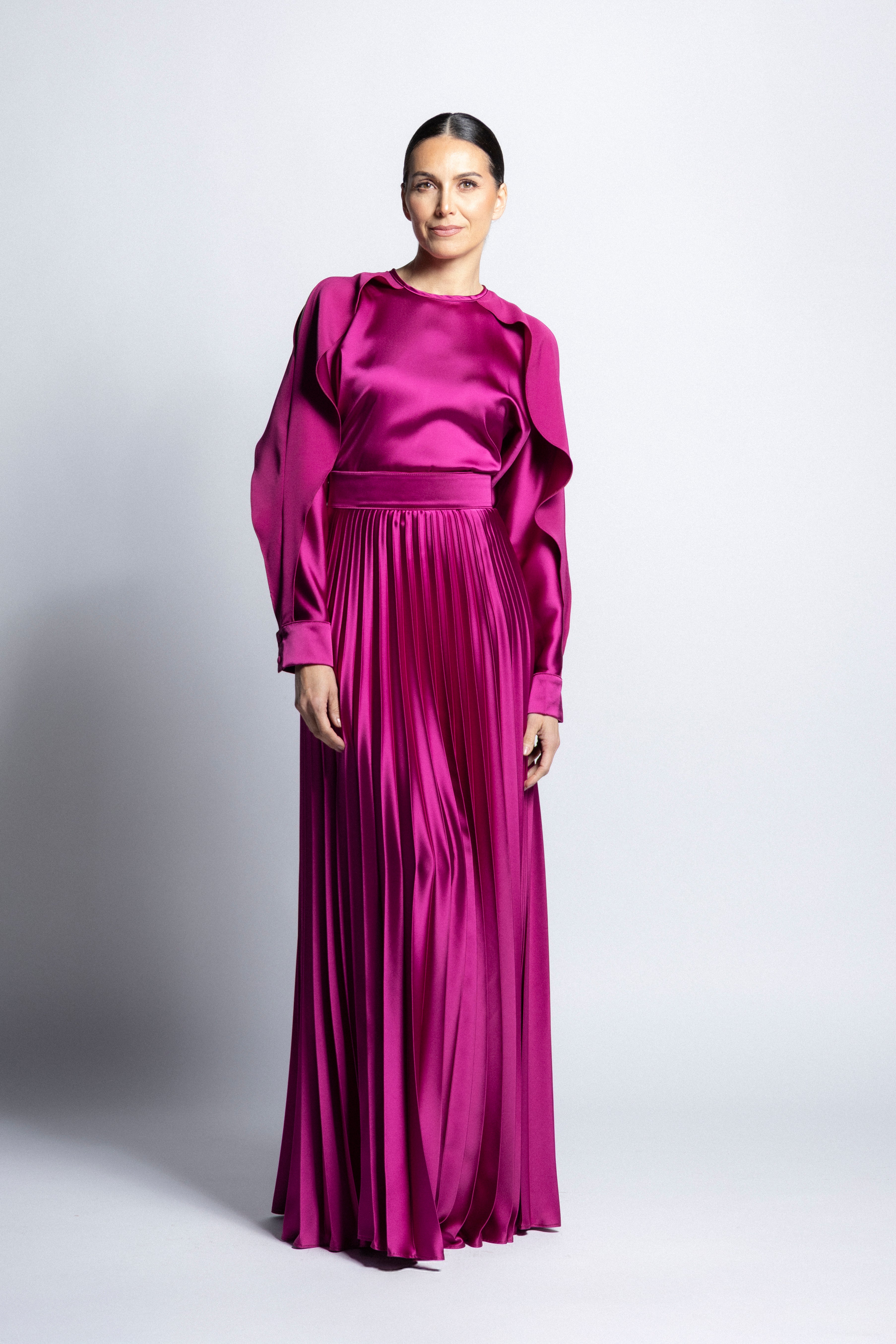 Vestido largo de satín en color bugambilia con torso de cuello redondo, mangas largas con puños detallados y falda larga plisada.