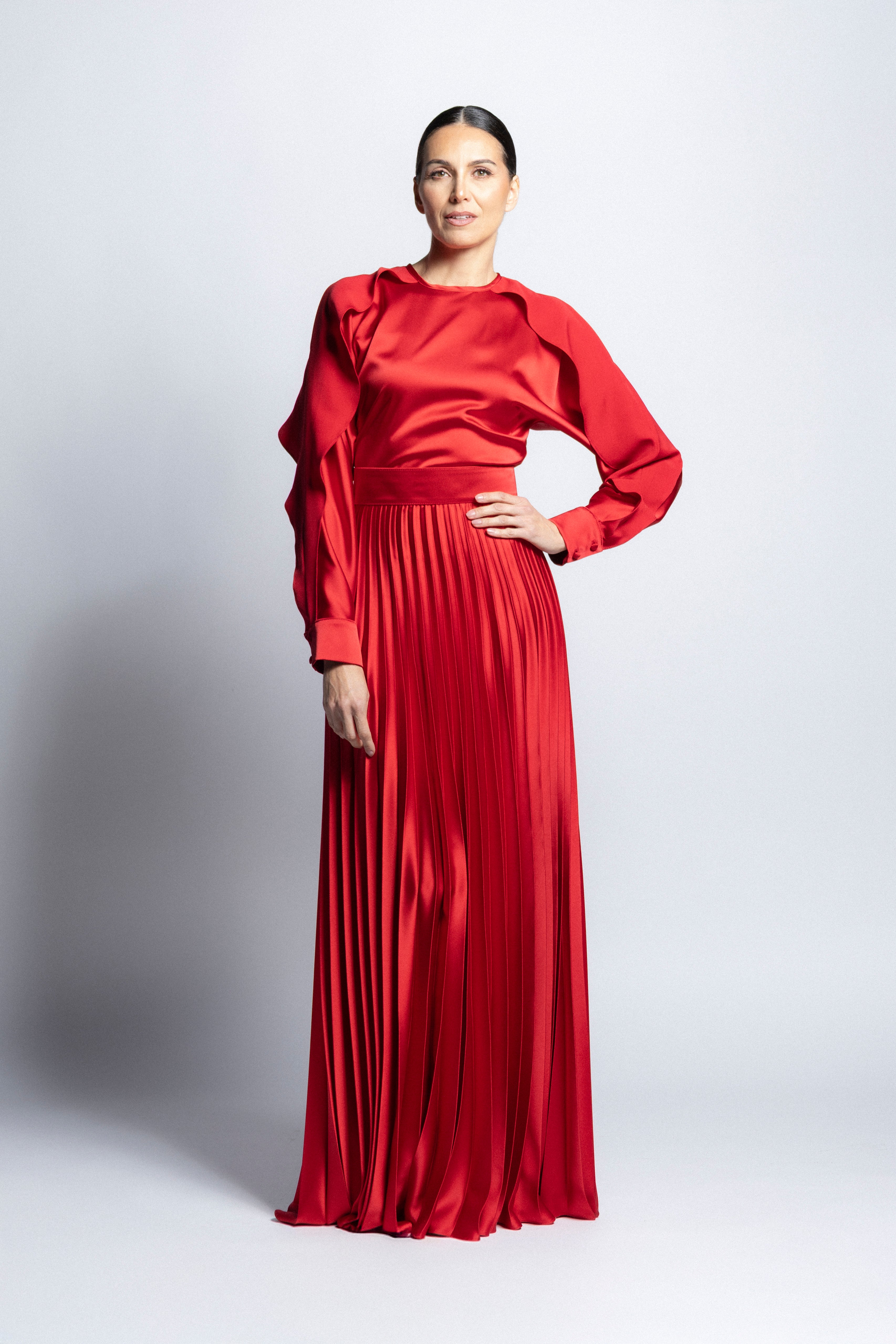 Vestido largo de satín en color rojo con torso de cuello redondo, mangas largas con puños detallados y falda larga plisada.
