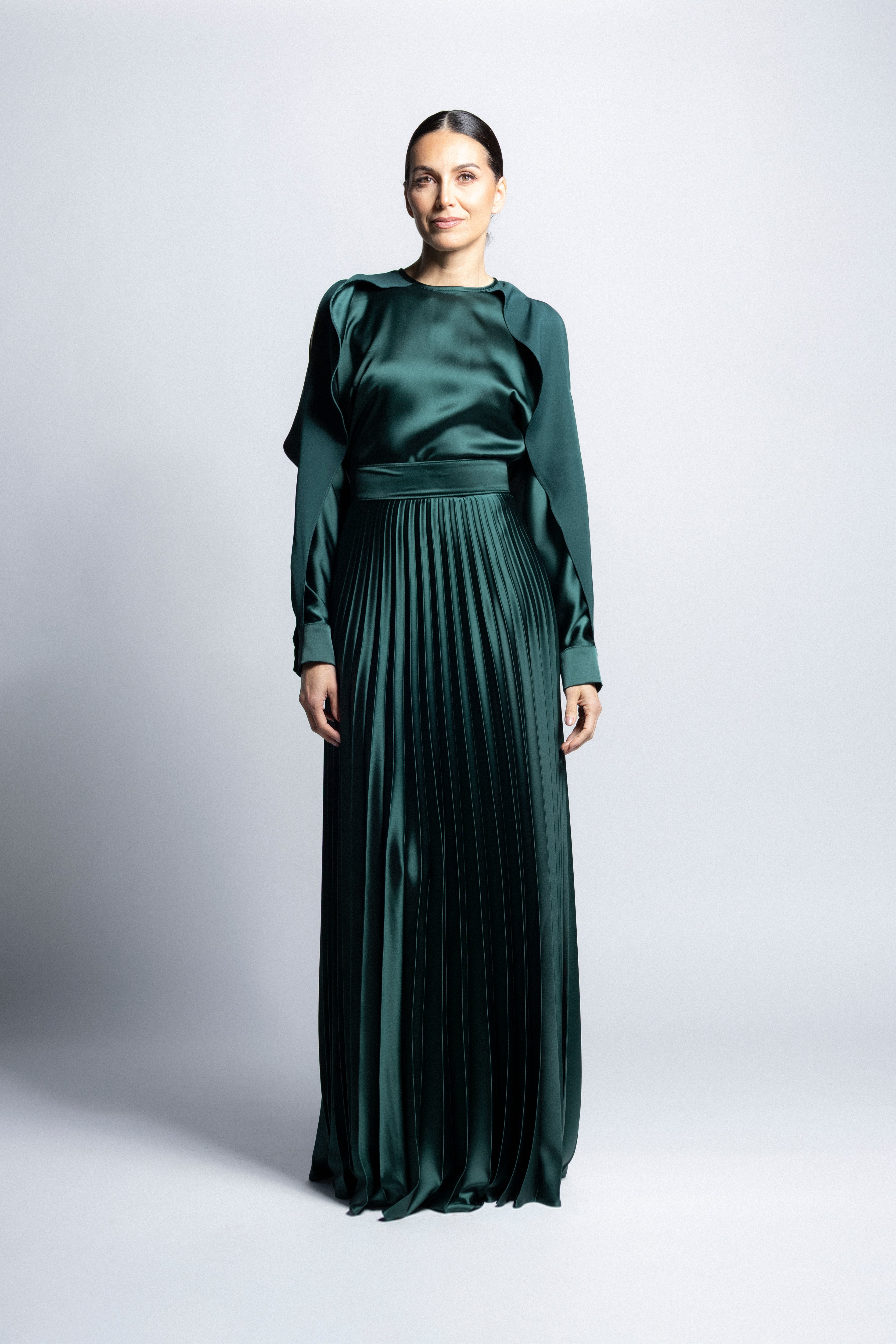 Vestido largo de satín en color verde con torso de cuello redondo, mangas largas con puños detallados y falda larga plisada.